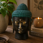 Large Antique Brass Buddha Head with a serene expression, featuring a teal patina on the hair, placed on a wooden surface surrounded by calming decor elements.