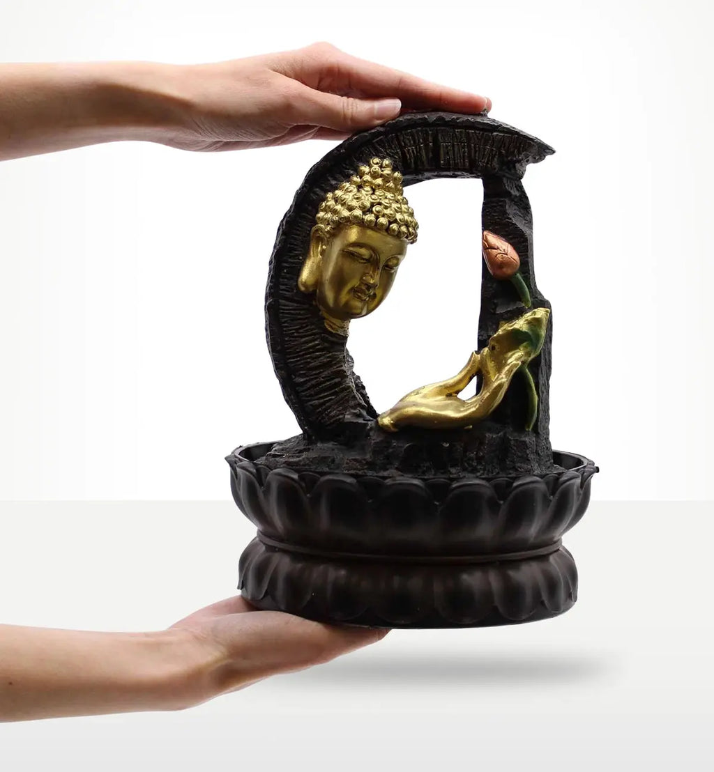 Hands holding a Tabletop Water Feature - 30cm - Golden Buddha & Lotus with a black base, golden Buddha head, and lotus flower detail in a serene design.