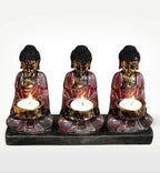 Antique Buddha - Three Devotees Candle Holder featuring three hand-carved Buddha statues holding lit candles, with an antique gold and red finish on a black base.
