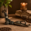 Antique Buddha - Hand Incense Burner featuring a detailed aged bronze hand sculpture holding a small candle, with a seated Buddha figure on the wrist, set in a warm ambient space.