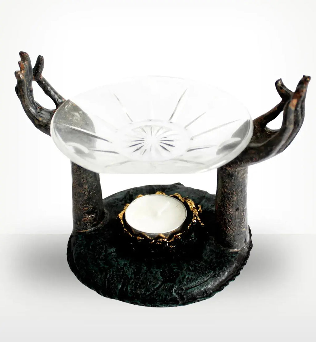 Antique Buddha - Om Hands Oil Burner featuring two sculpted hands in a meditative gesture supporting a glass dish above a tealight candle holder in a rustic dark finish.
