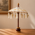 Decorative Bali Home Decor Parasol - Canvas - Gold Decor- 40cm with intricate gold patterns and hanging tassels, displayed on a wooden stand next to candles and glassware.