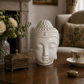 Buddah Head Oil Burner - White made of smooth ceramic with a serene expression, releasing gentle smoke, placed on a wooden table in a cozy, elegantly decorated living room.