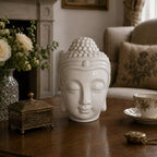 Buddah Head Oil Burner - White made of smooth ceramic with a serene expression, releasing gentle smoke, placed on a wooden table in a cozy, elegantly decorated living room.
