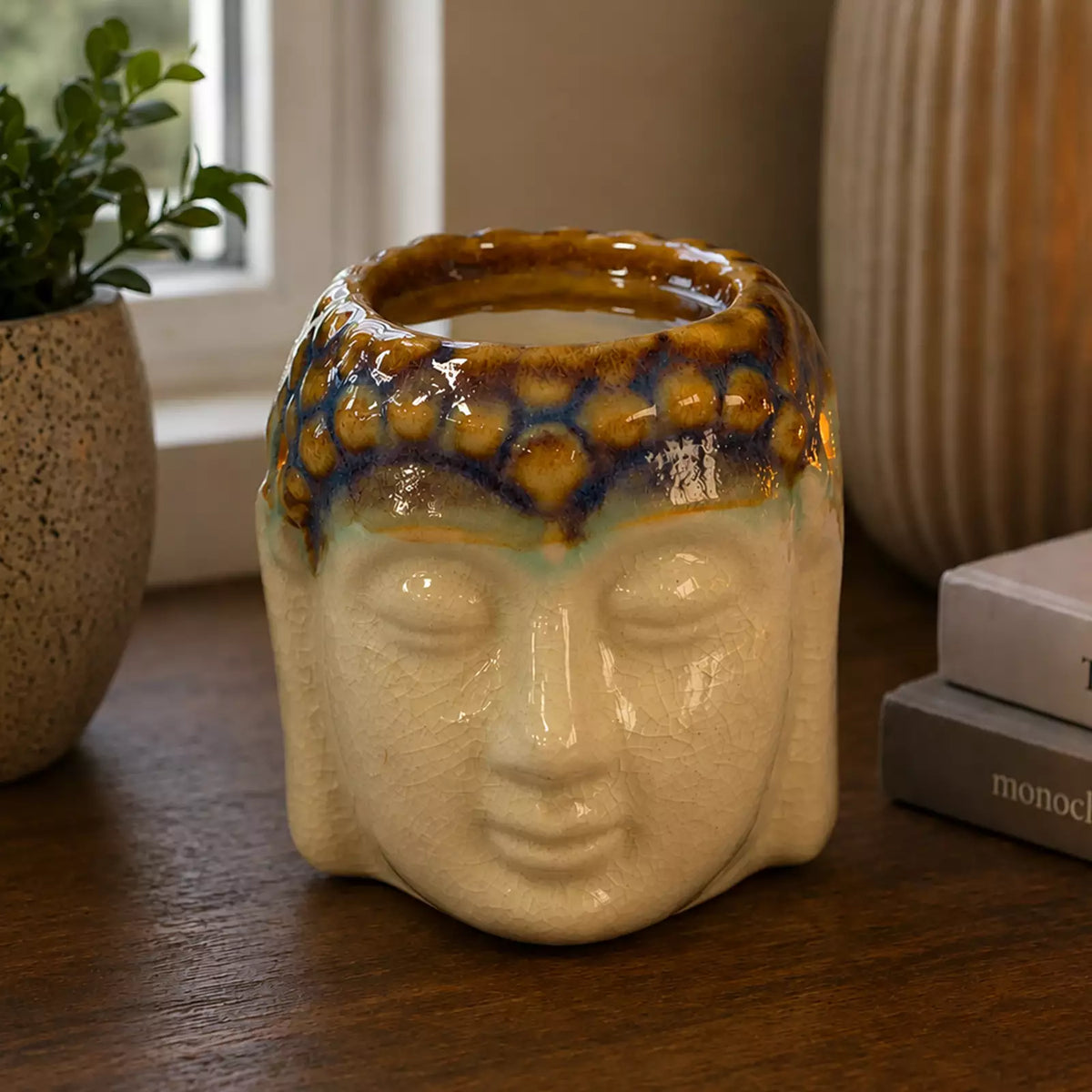 Buddha Oil Burner - Ivory & Mint ceramic oil burner shaped like a Buddha head with a lit flame, placed on a wooden surface near books and decorative candles.
