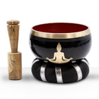 Buddha Singing Bowl Set- Black/Orange 10.7cm featuring a black bowl with a gold Buddha silhouette, accented with a brass rim, seated on a cushion with silver stripes and accompanied by a wooden striker.