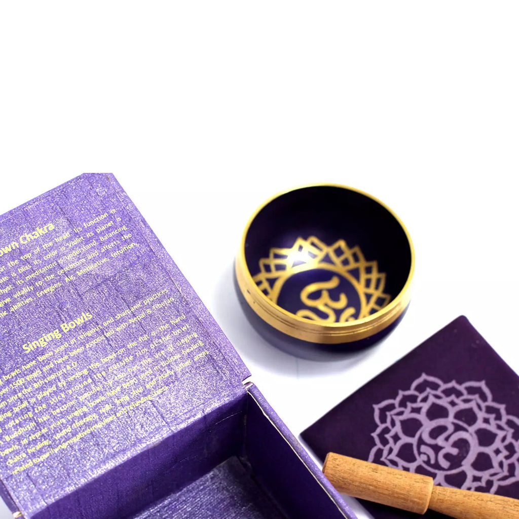 Singing bowl with gold interior and lid, placed on a white surface next to an open purple box.