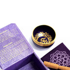 Singing bowl with gold interior and lid, placed on a white surface next to an open purple box.