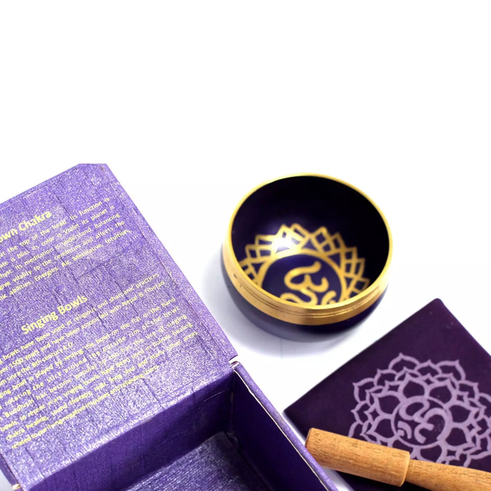 Singing bowl with gold interior and lid, placed on a white surface next to an open purple box.