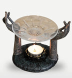 Antique Buddha - Om Hands Oil Burner featuring two sculpted hands holding a clear glass dish above a lit tealight candle on a textured dark base, creating a serene ambiance.