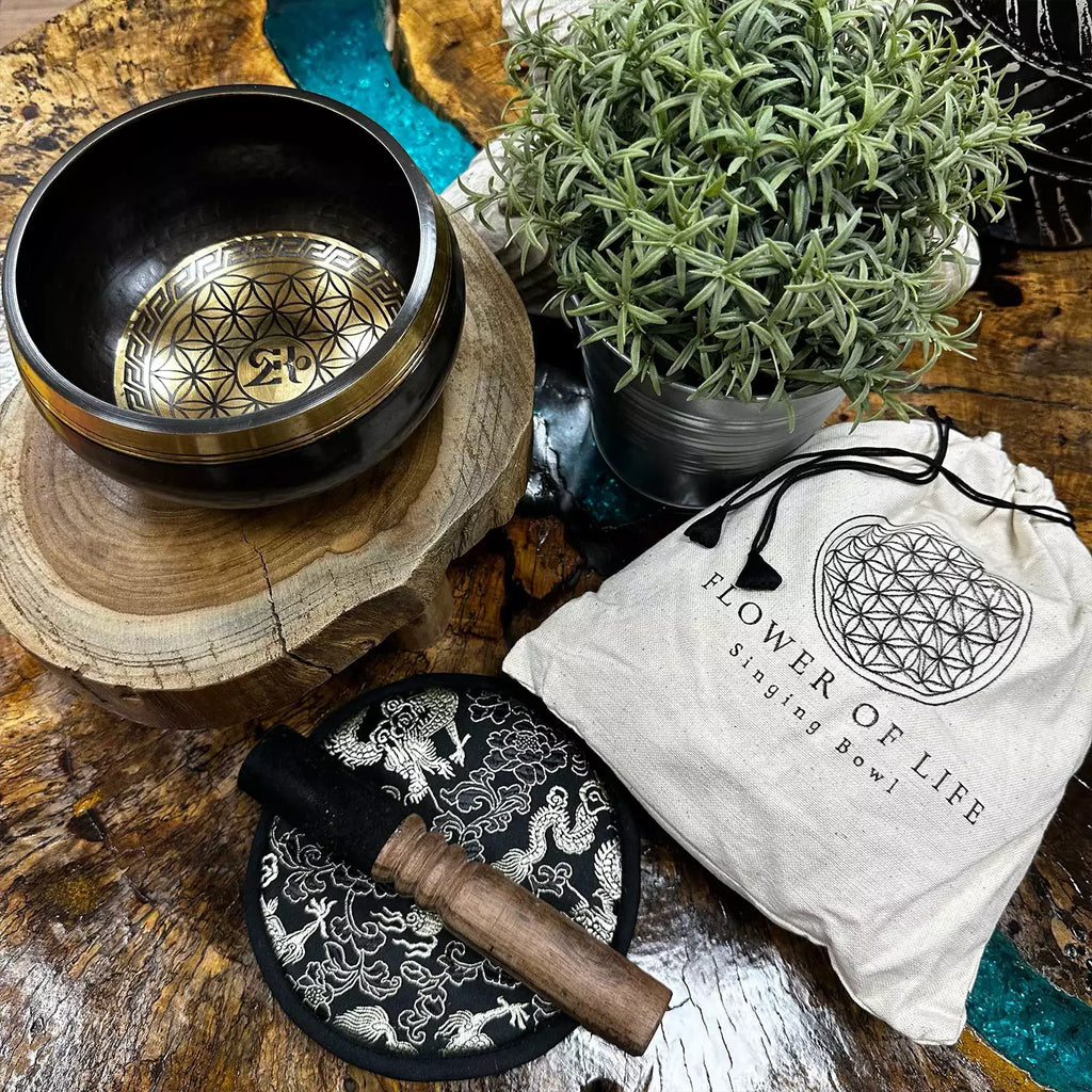 Singing bowl set with 'Flower of Life' design on a wooden surface with a plant and pouch.