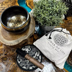 Singing bowl set with 'Flower of Life' design on a wooden surface with a plant and pouch.