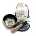 Singing bowl set with decorative plate and cleaning stick, accompanied by a 'Green Tara' branded bag on a white background.