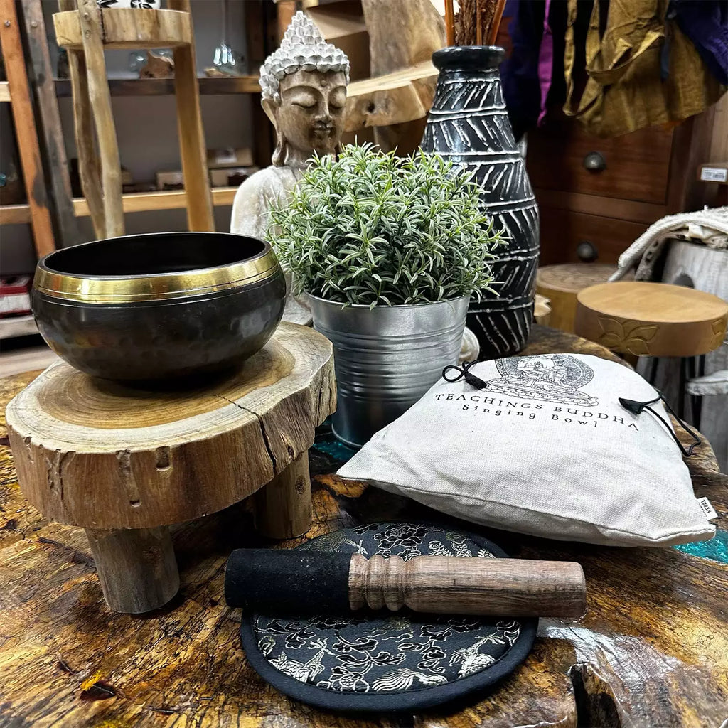 Meditation items including a singing bowl, Buddha statue, and potted plant on a wooden surface.