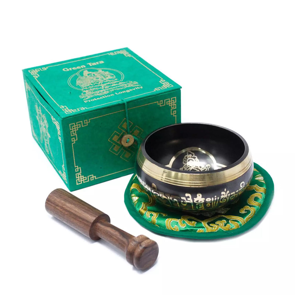 A Tibetan singing bowl set on a white background, including a black and gold singing bowl on a green decorative cushion, a wooden mallet, and a green branded box.