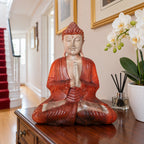 40 cm wooden Buddha with hands in prayer on a dark hall cabinet beside a red-carpeted staircase.