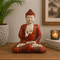 Hand Carved Wooden Buddha Statue - 30cm Teaching Transmission seated in meditation with detailed red robes, placed on a wooden surface beside a candle, plant, and framed artwork.