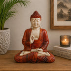 Hand Carved Wooden Buddha Statue - 30cm Teaching Transmission seated in meditation with detailed red robes, placed on a wooden surface beside a candle, plant, and framed artwork.
