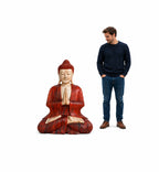 A man standing beside a large Hand Carved Wooden Buddha Statue - 30cm Welcome, featuring a serene meditative pose with red and natural wood tones.