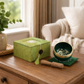 A green marbled singing bowl set with a wooden mallet and matching box, styled on a wooden table in a cozy living room setting.