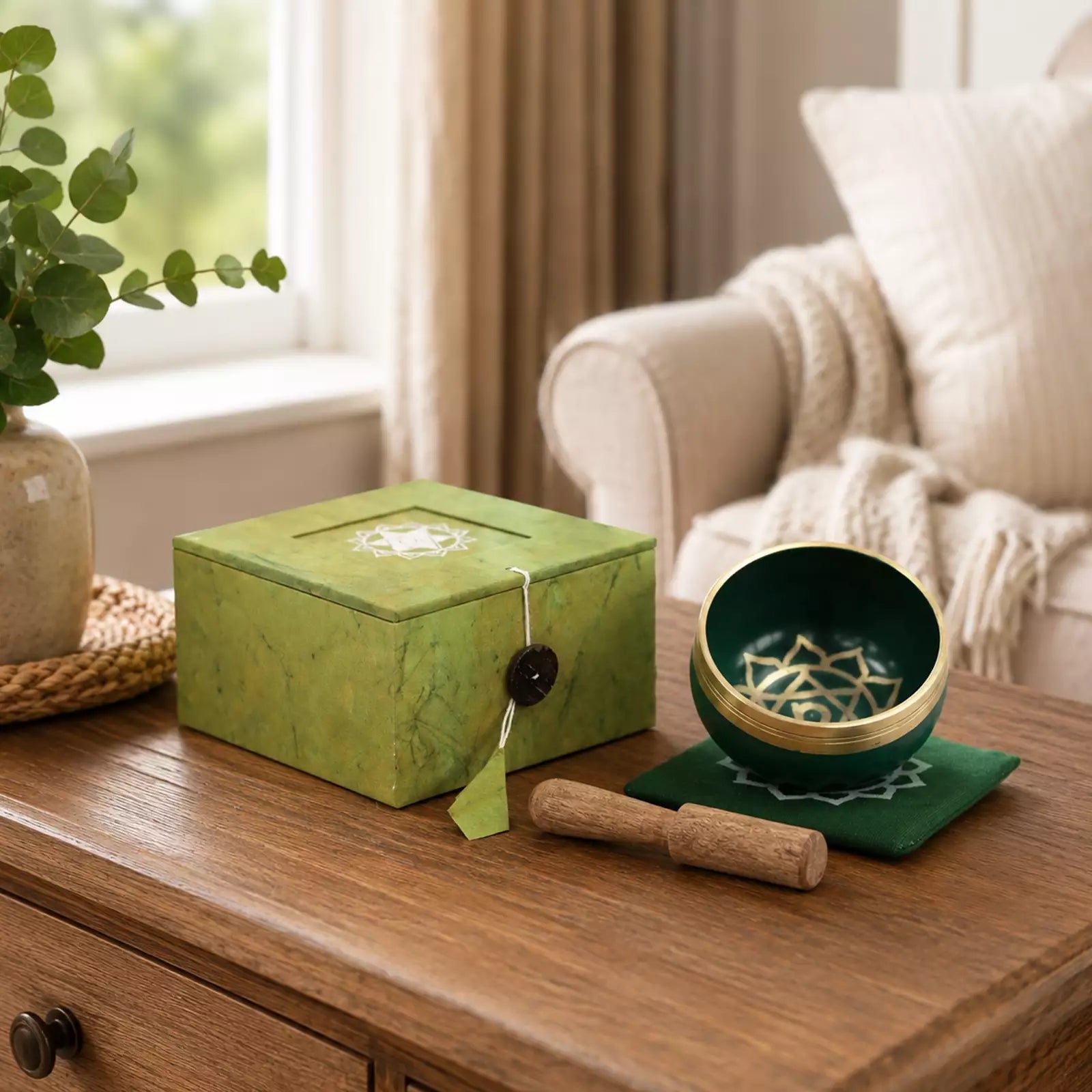 A green marbled singing bowl set with a wooden mallet and matching box, styled on a wooden table in a cozy living room setting.