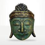 A decorative Buddha head sculpture with a textured green patina finish and gold accents on the crown and forehead, shown against a light gray gradient background.