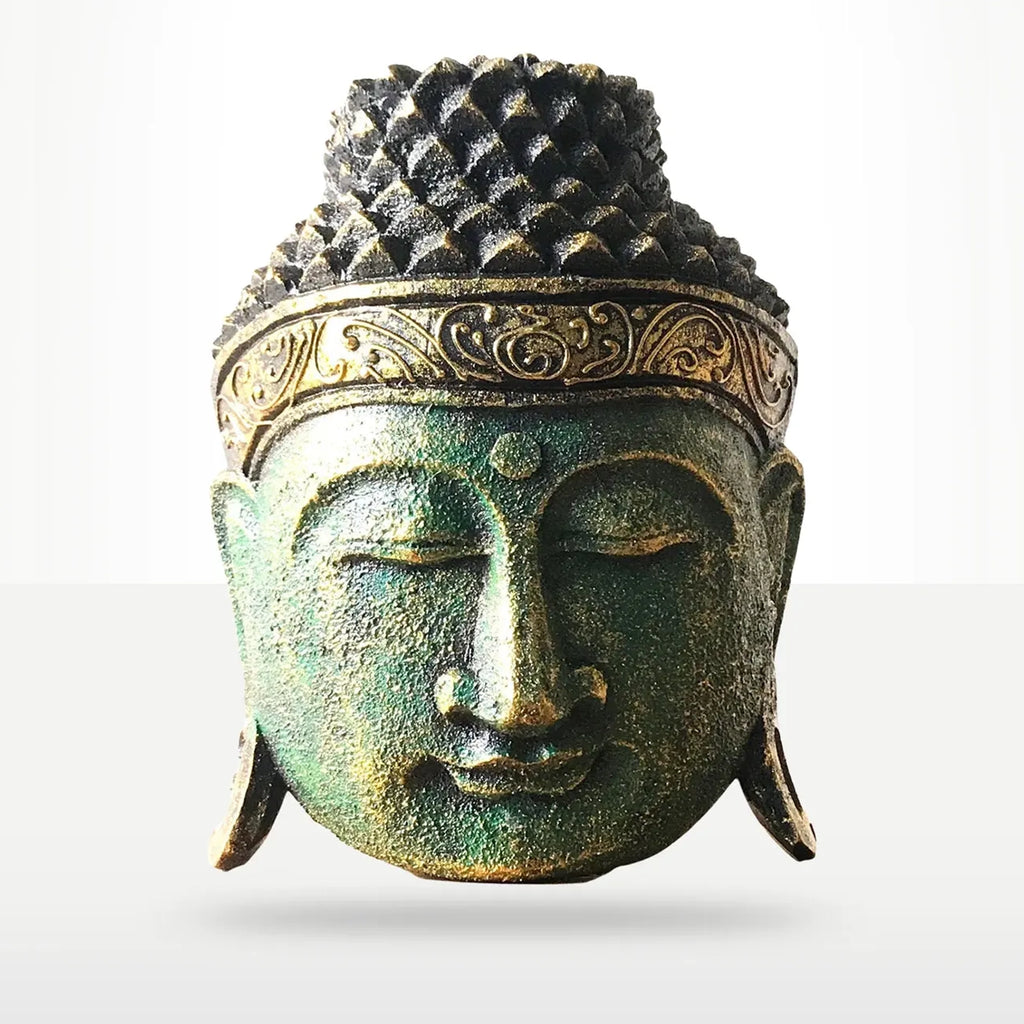 A decorative Buddha head sculpture with a textured, weathered finish in greenish-bronze tones and gold accents on the crown band, shown against a light gray gradient background.