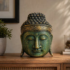 A decorative Buddha head sculpture with a textured green and gold finish, displayed on a wooden cabinet in a styled home interior setting.