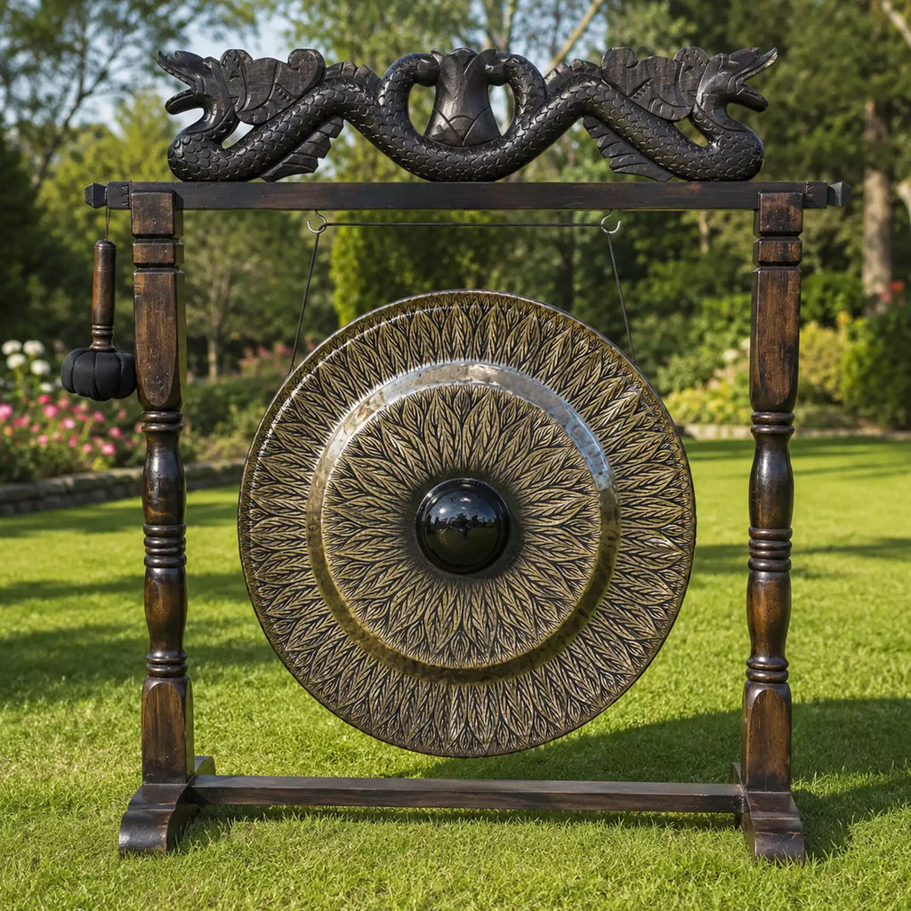 A large decorative outdoor gong with an ornate wooden stand, featuring a dragon motif at the top and a hanging mallet, set on a green lawn with trees in the background.