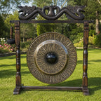 A large decorative outdoor gong with an ornate wooden stand, featuring a dragon motif at the top and a hanging mallet, set on a green lawn with trees in the background.