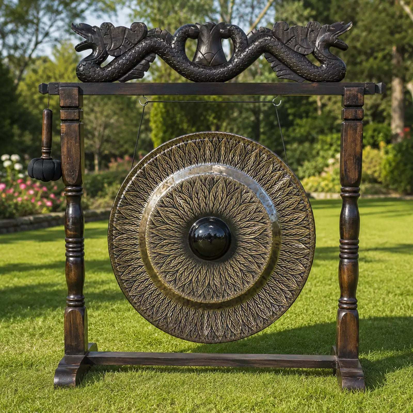 A large decorative outdoor gong with an ornate wooden stand, featuring a dragon motif at the top and a hanging mallet, set on a green lawn with trees in the background.
