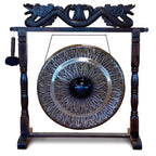 A large decorative gong with an engraved floral or leaf-like pattern, mounted on a dark wooden stand with carved dragon-like details at the top and a hanging mallet on the left, shown against a plain white background.