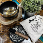 Tibetan singing bowl set with wooden striker, pouch, and plant on a wooden surface
