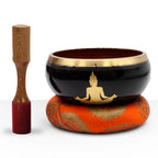 Large Buddha Singing Bowl Set- Black/Orange 14cm featuring a black and gold bowl with a Buddha figure, resting on an orange cushion, accompanied by a wooden mallet.