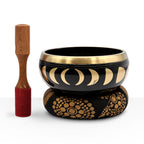 Large Moon Phase Singing Bowl Set- Black 14cm with gold moon phase design, wooden striker with red suede tip, resting on patterned cushion for meditation and sound healing.