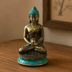 A small seated Buddha statue with an antique gold finish and turquoise patina accents on the head and base, displayed on a wooden surface.
