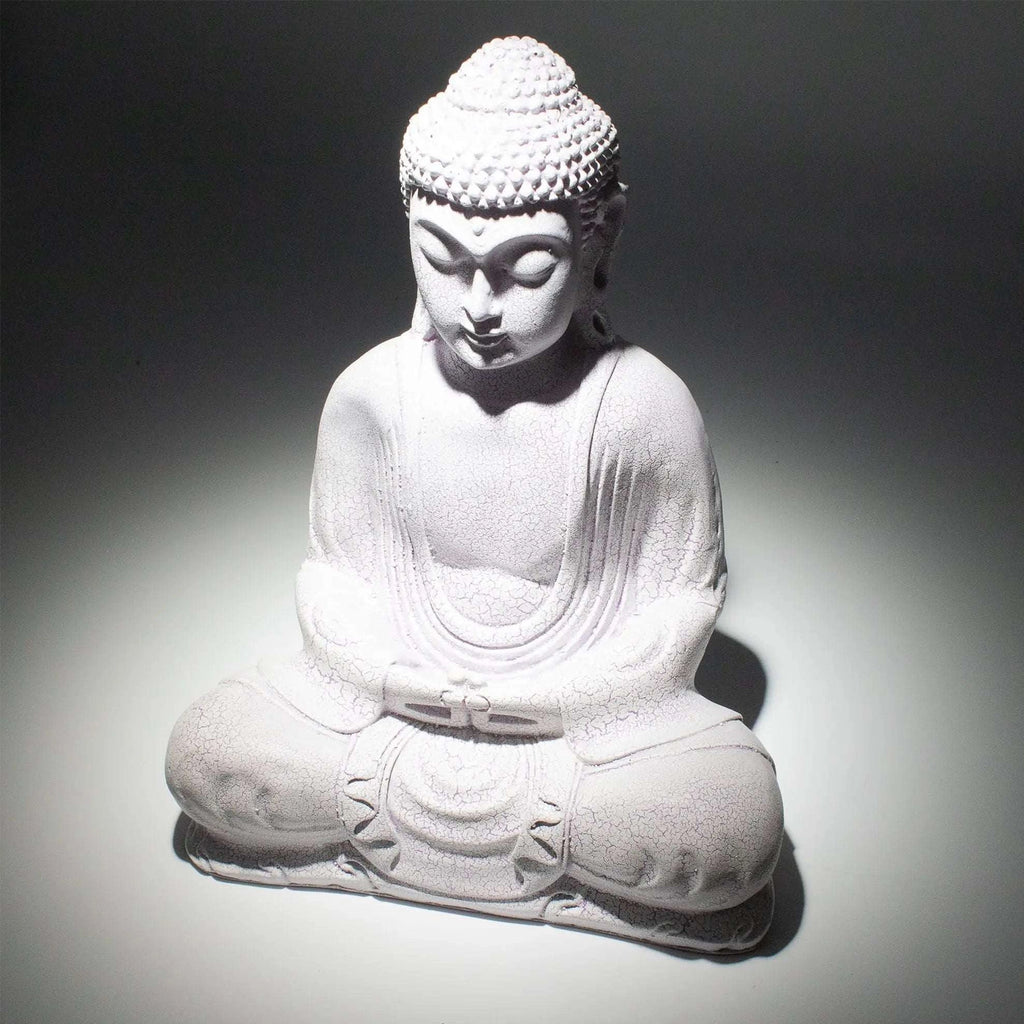 A white seated Buddha statue with a textured stone-like finish, photographed against a dark gray to white spotlight background.
