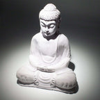 A white seated Buddha statue with a textured stone-like finish, photographed against a dark gray to white spotlight background.