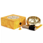 Brass singing bowl with wooden striker and yellow box on a white background