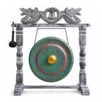 A decorative gong with a distressed gray wooden frame and a round green patinated metal drum head featuring a gold center, shown on a white background with a hanging mallet.