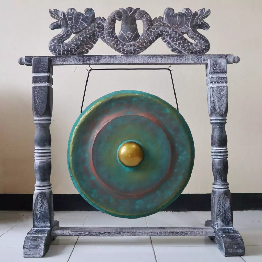 A large round gong with a green and blue patina finish and a gold-colored center, mounted on a dark gray carved wooden frame with dragon details at the top.