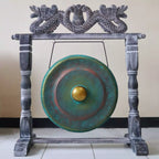 A large round gong with a green and blue patina finish and a gold-colored center, mounted on a dark gray carved wooden frame with dragon details at the top.