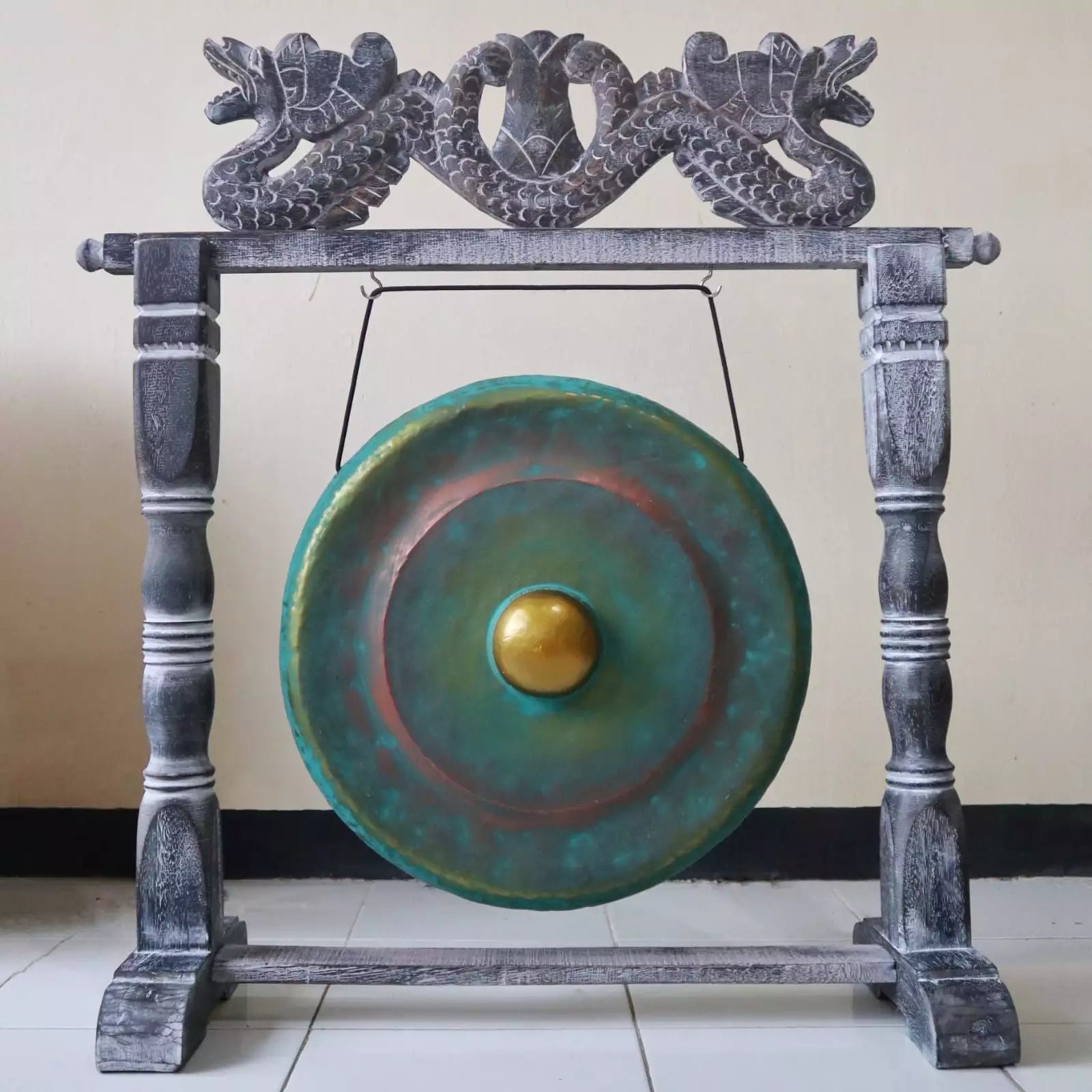 A large round gong with a green and blue patina finish and a gold-colored center, mounted on a dark gray carved wooden frame with dragon details at the top.