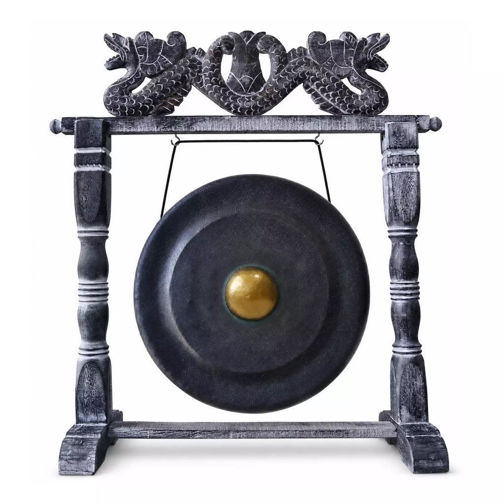 A large round black gong with a gold-colored central boss, suspended from a dark wooden stand featuring ornate dragon carvings at the top, isolated on a white background.