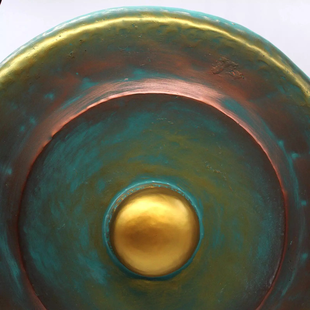 Close-up of a round ceramic bowl or planter with a textured metallic finish, featuring concentric rings of teal, copper-brown, and a central gold accent.