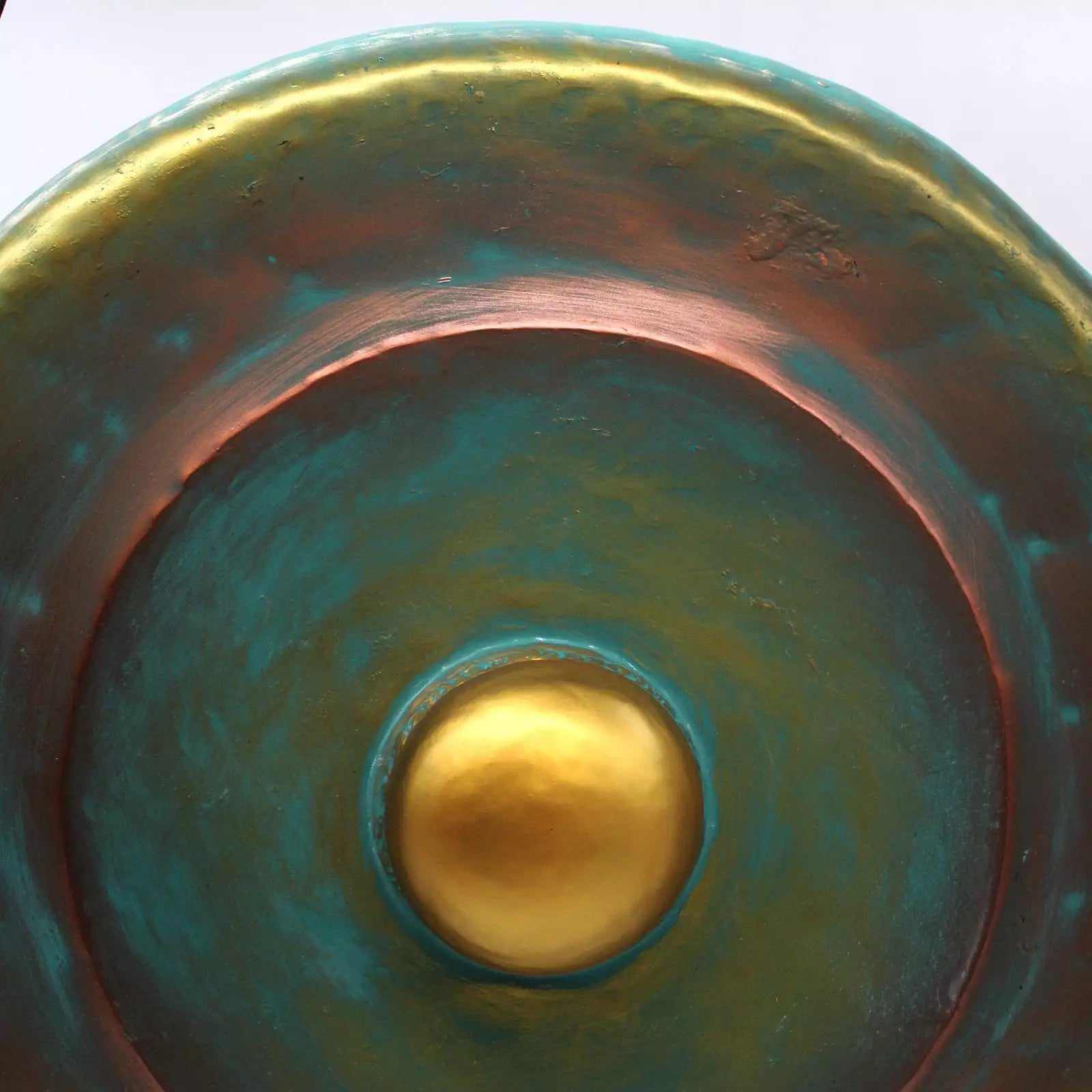 Close-up of a round ceramic bowl or planter with a textured metallic finish, featuring concentric rings of teal, copper-brown, and a central gold accent.
