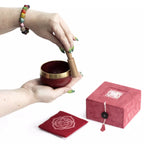 Red singing bowl with gold interior, wooden striker, and red box on a white background
