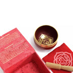 Red singing bowl set with a gold bowl and wooden stick on a white background
