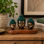 Set of 3 - Buddha Heads (asst sizes) displayed on a wooden base with green textured hair, placed on a wooden table next to a plant and books, ideal for Buddha decor.