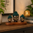 Set of 3 - Buddha Heads (asst sizes) displayed on a wooden base with dark green knitted caps, featuring hand carved brass Buddha head statues arranged on a wooden surface with warm ambient lighting.